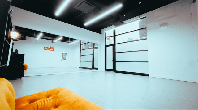 Dance studio from the perspective of a stylish orange couch in the back corner, highlighting the expansive mirrors in the front and cubbies on the side