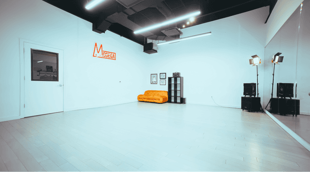 Dance studio from the perspective of the front corner, highlighting the sprung wood dance floor, cubbies, stylish couch, spotlight and speakers