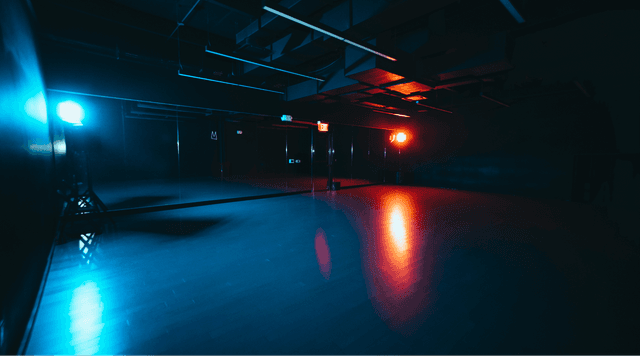 Large, column-free dance studio with blue lighting and expansive mirrors